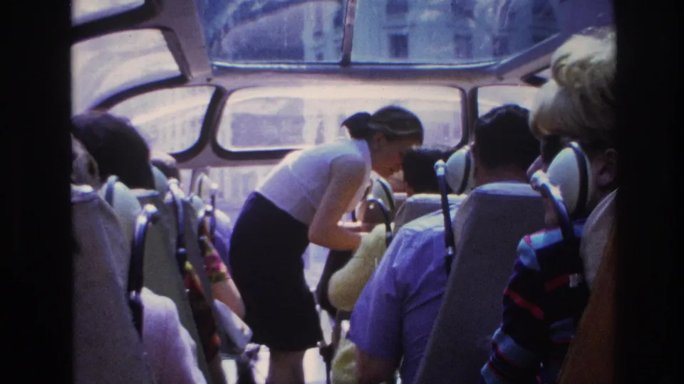 Paris 1967 sightseeing bus scene with seated tourists, curved windows, and a woman bending beside a passenger in the upper tier.