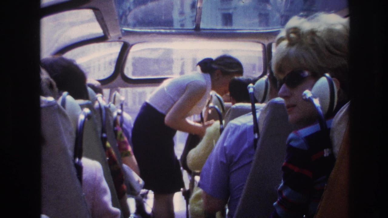 1967 Paris home-movie frame showing passengers inside a curved glass-roof bus, with a woman in white moving between seats.