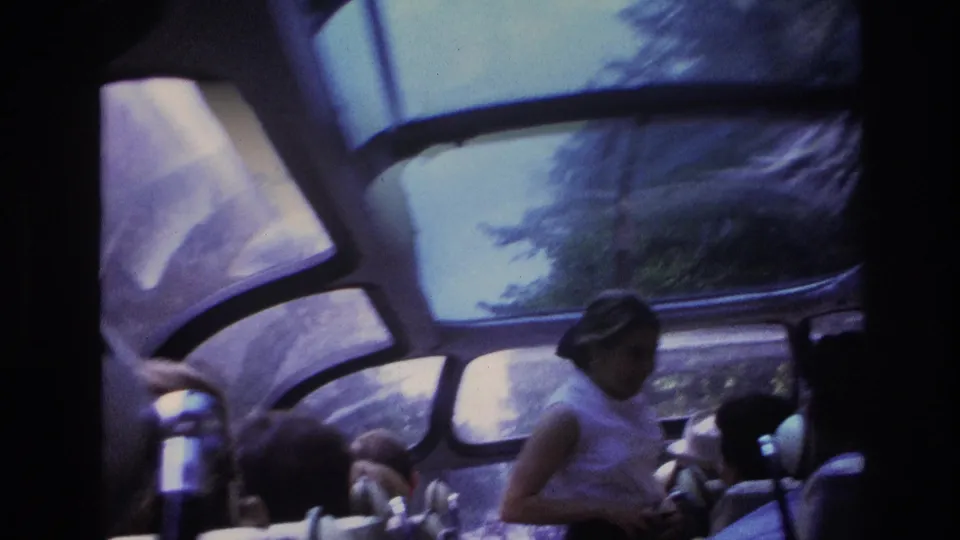 1967 Paris home-movie view inside a glass-roof bus, showing passengers seated as trees pass outside the windows.