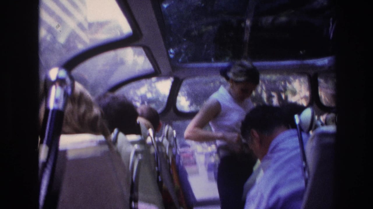 1967 Paris home-movie frame showing bus passengers, curved windows, and a woman in a white top near the aisle.