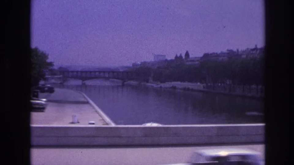 Paris river view from a moving bus, showing the Seine, a bridge, embankments, trees, and blurred passing traffic.