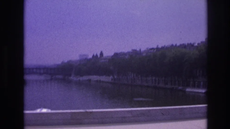 Final 1967 Paris bus-window view of the Seine area, with soft focus, bridge span, trees, and riverside embankment.