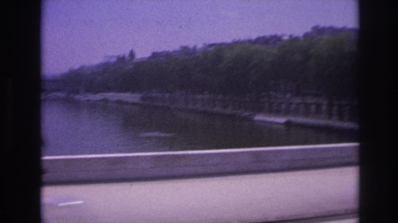 1967 Paris riverside view from a moving vehicle, with water, embankment trees, road barrier, and dark window framing.