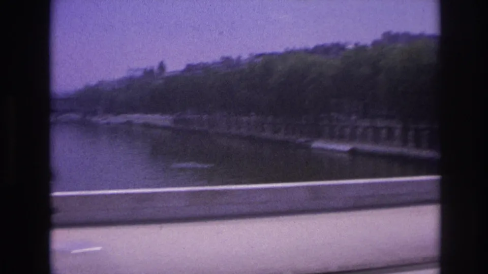 1967 Paris riverside view from a moving vehicle, with water, embankment trees, road barrier, and dark window framing.
