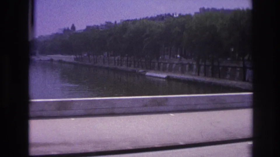 1967 Paris home-movie view of a waterway and tree-lined embankment, filmed from a moving vehicle with soft blur.