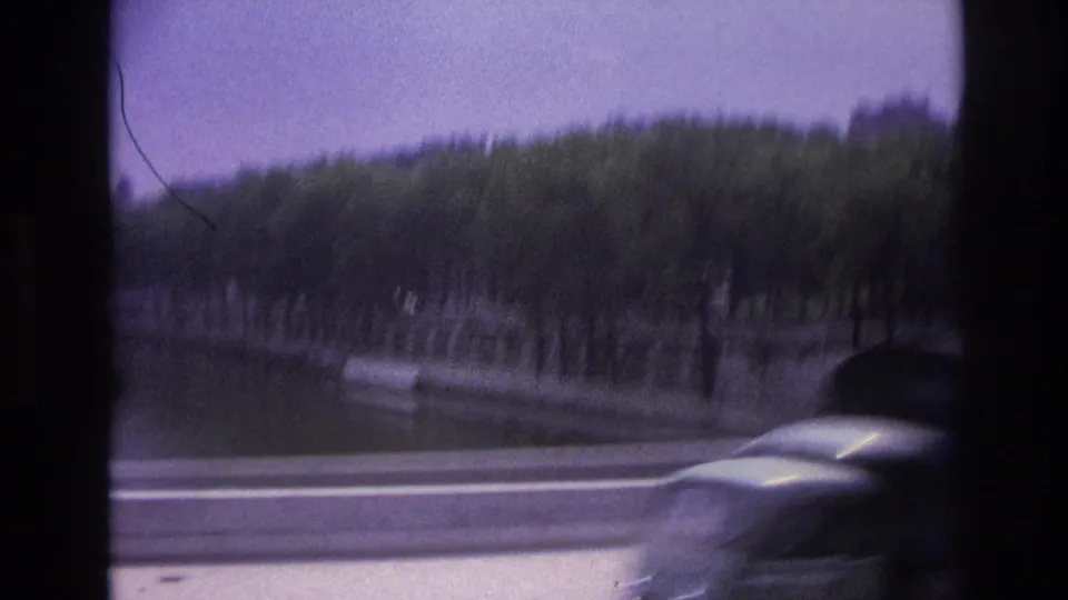 1967 Paris frame with a passing car in the foreground and a tree-lined waterway beyond the roadside barrier.