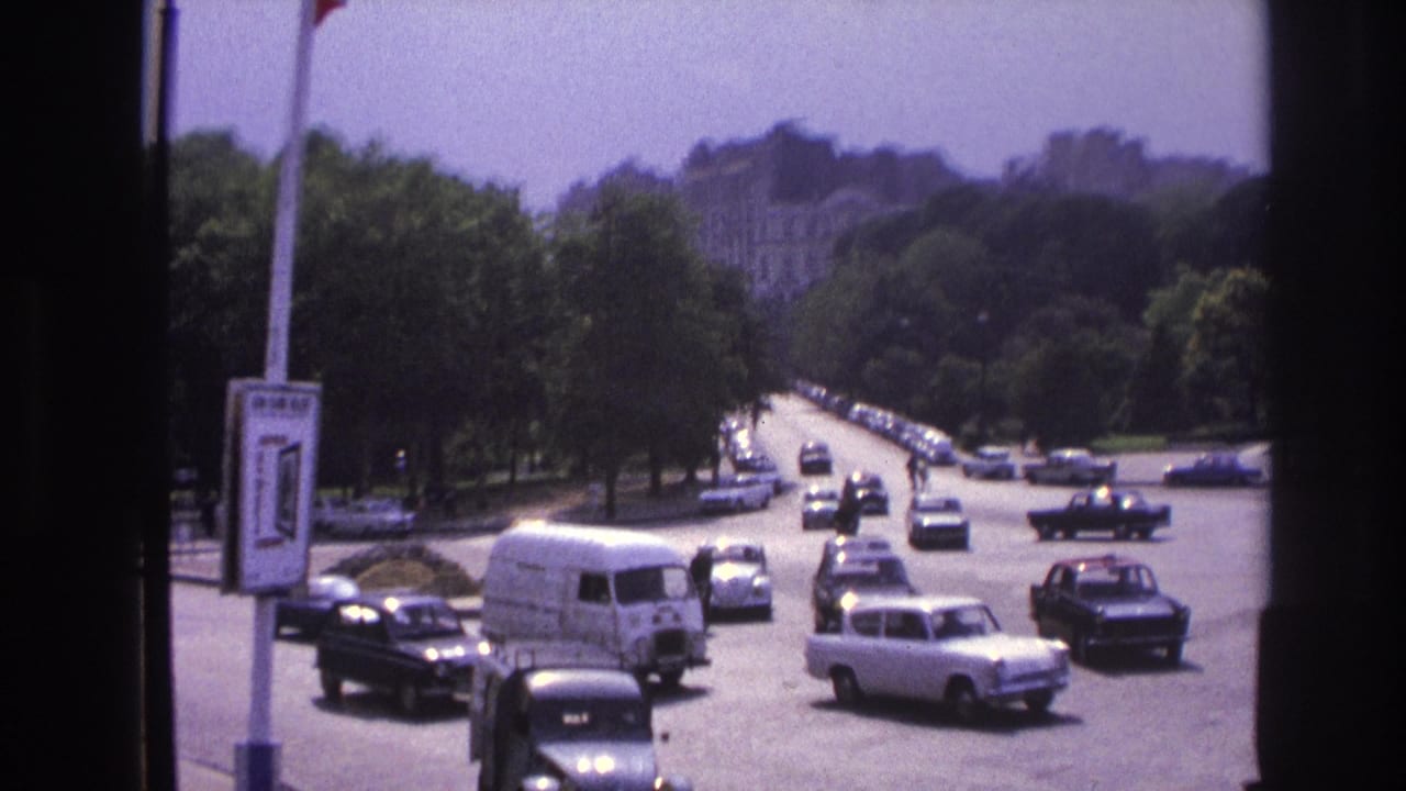 1967 Paris home-movie view of cars and a white van moving through a broad, tree-lined street area.