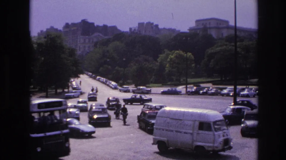 1967 Paris street traffic with a bus at left, white van in front, pedestrians, and cars crossing the open road.