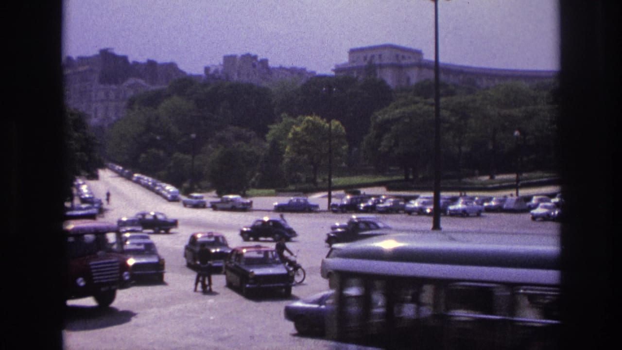 1967 Paris street view with moving and parked period cars, pedestrians, trees, and a large building beyond the roadway.