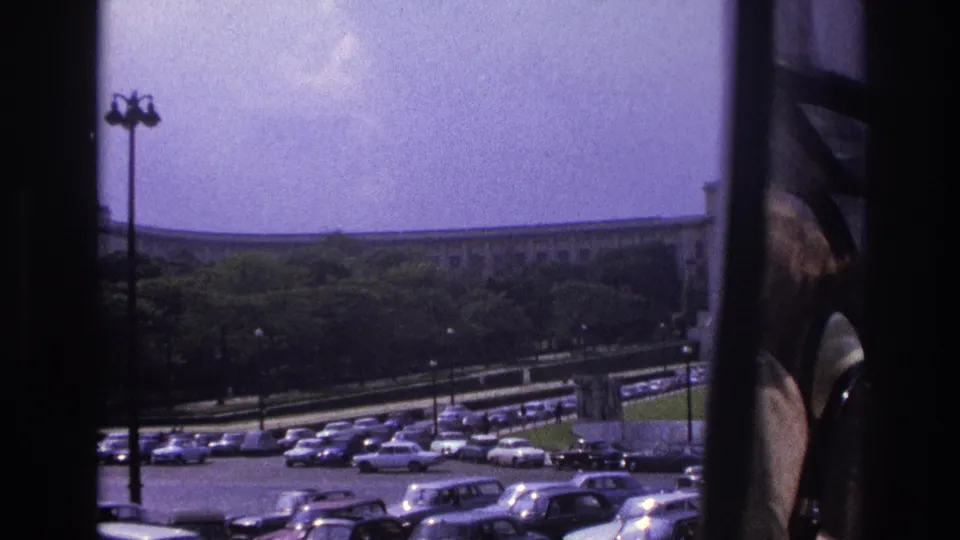 1967 Paris home-movie view of parked cars, a foreground lamppost, trees, and a long building, with the camera partly blocked by a window frame.