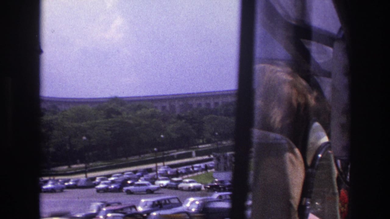 1967 Paris home-movie frame showing the Eiffel Tower area through dark vehicle window frames, with cars and trees below.