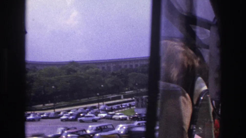 1967 Paris home-movie frame showing the Eiffel Tower area through dark vehicle window frames, with cars and trees below.