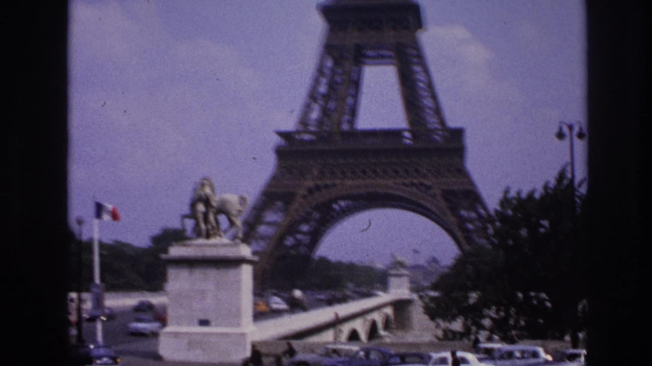 1967 Paris frame with the Eiffel Tower rising behind an equestrian statue, French flag, bridge, and moving cars.