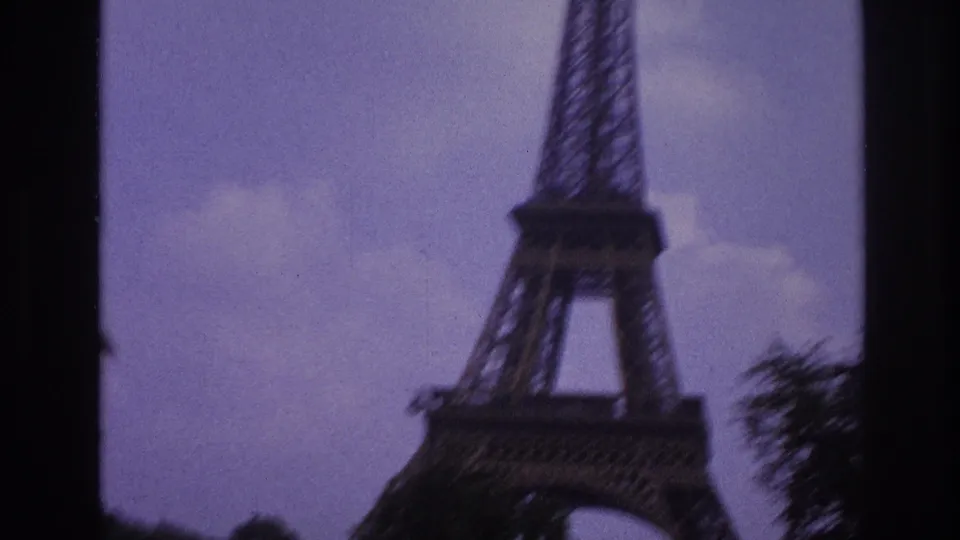 Soft 1967 Paris frame of the Eiffel Tower seen from below, with trees and dark film-edge framing.