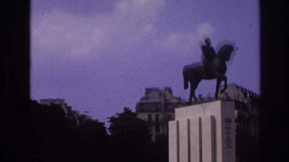 1967 Paris home-movie frame showing an equestrian statue on a pedestal, with trees and building facades in the background.