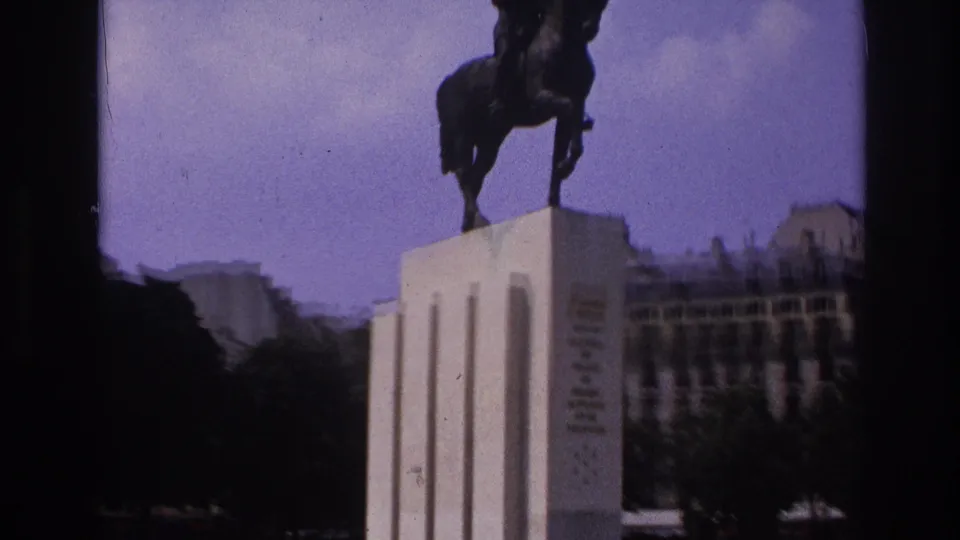 Paris travel-film frame with a closer handheld view of the equestrian monument silhouetted above a pale pedestal.