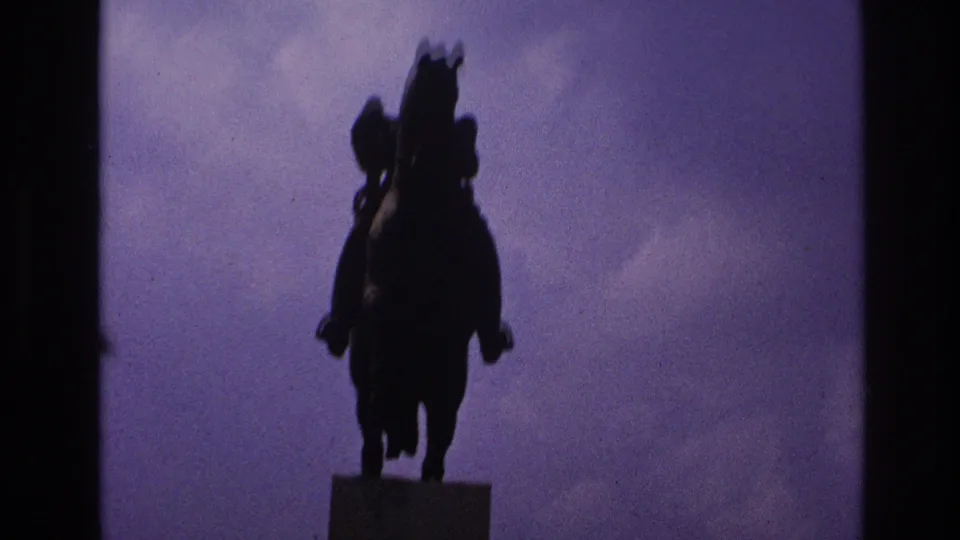 Front-facing home-movie view of the Paris equestrian monument, dark against the cloudy purple-blue sky.
