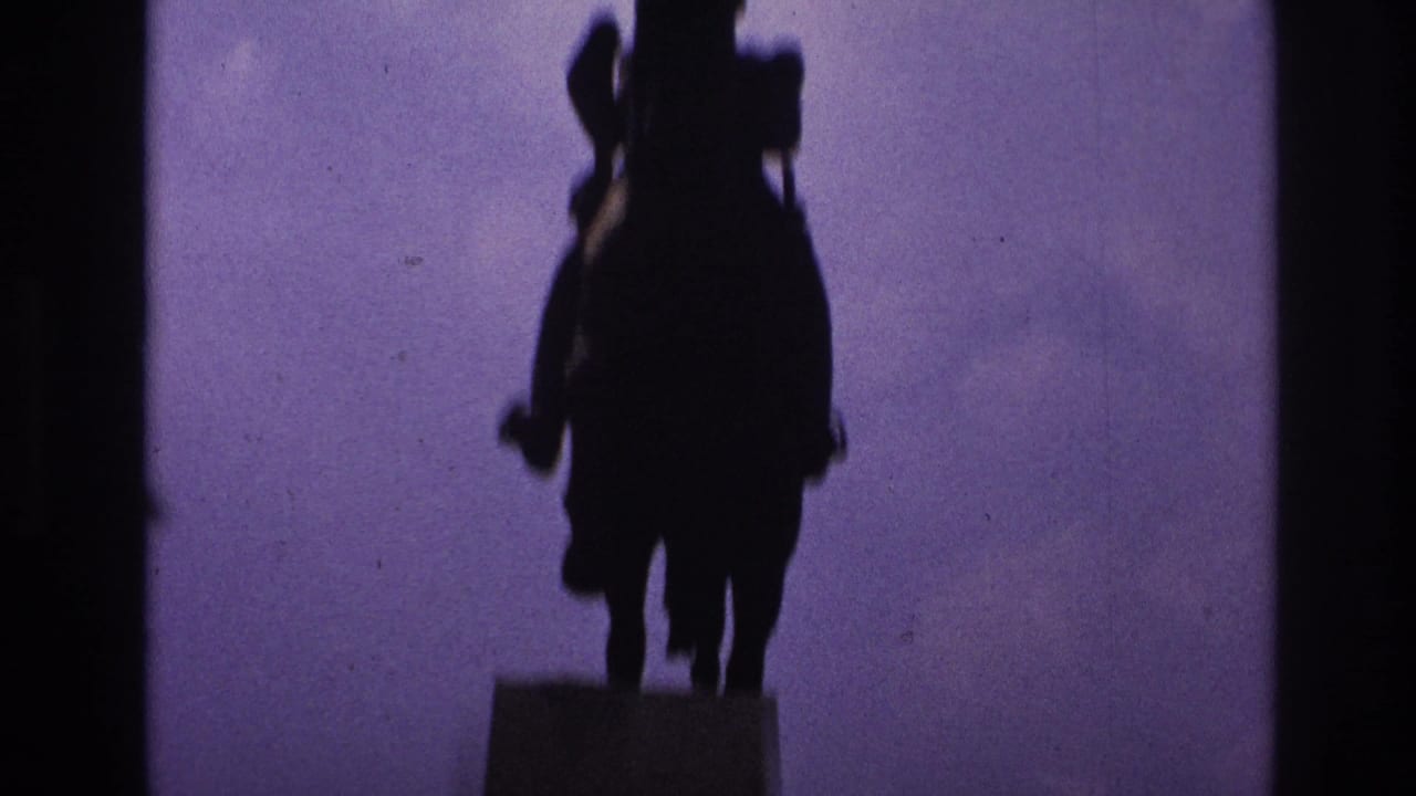 1967 Paris home-movie frame showing a silhouetted mounted statue above a dark park edge and purple sky.