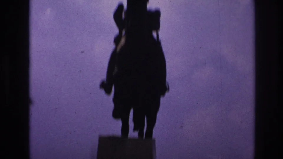 1967 Paris home-movie frame showing a silhouetted mounted statue above a dark park edge and purple sky.