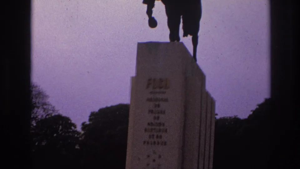 1967 Paris home-movie frame centered on the Foch pedestal, with the rider partly cropped above and park trees behind.