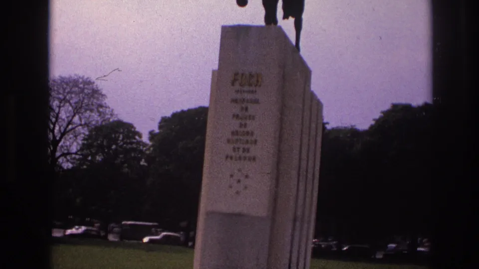 1967 Paris frame showing the full pedestal face of the Foch monument, with trees, grass, and distant parked cars visible.