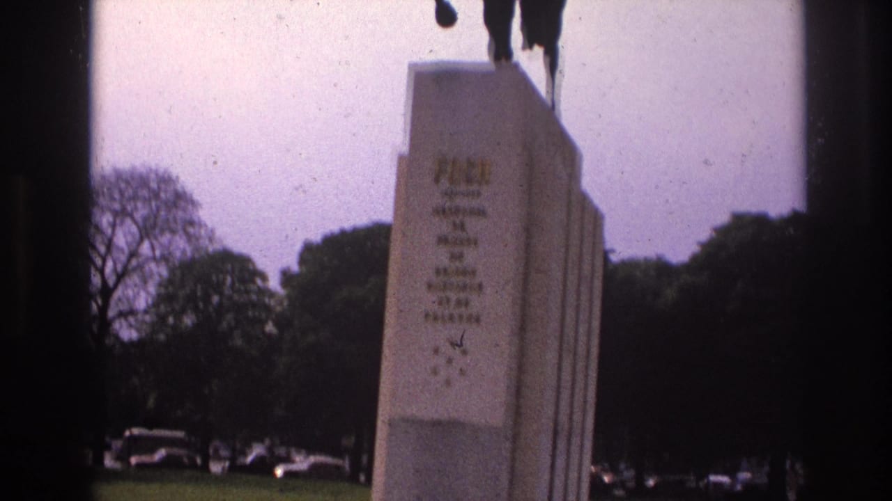 1967 Paris home-movie frame showing a horse statue on a stone pedestal, with grass, trees, and parked cars in the background.
