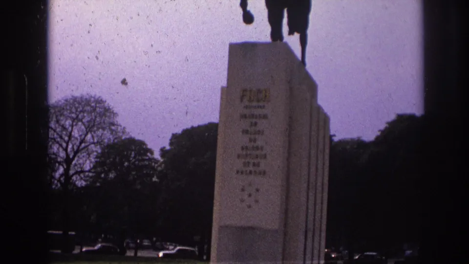 1967 Paris home-movie view of the monument pedestal, with partial statue legs above and dark trees behind.