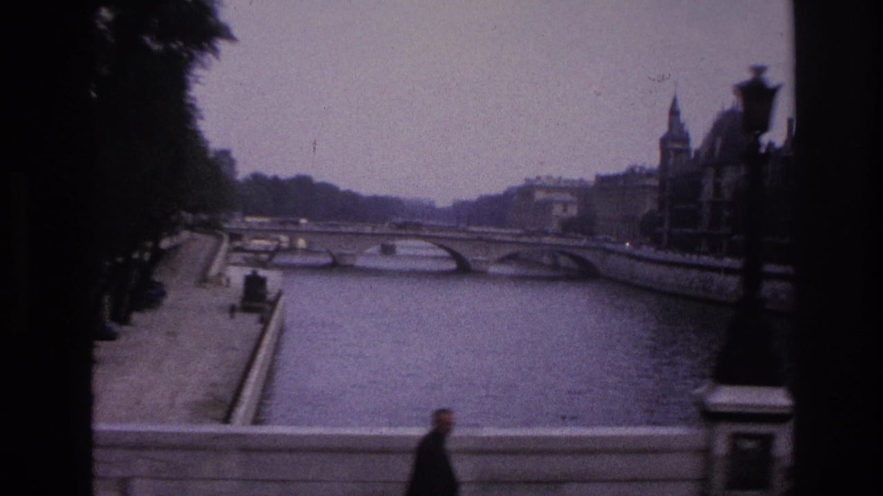 River view with an arched bridge, quay wall, lamppost, and pedestrian in foreground.