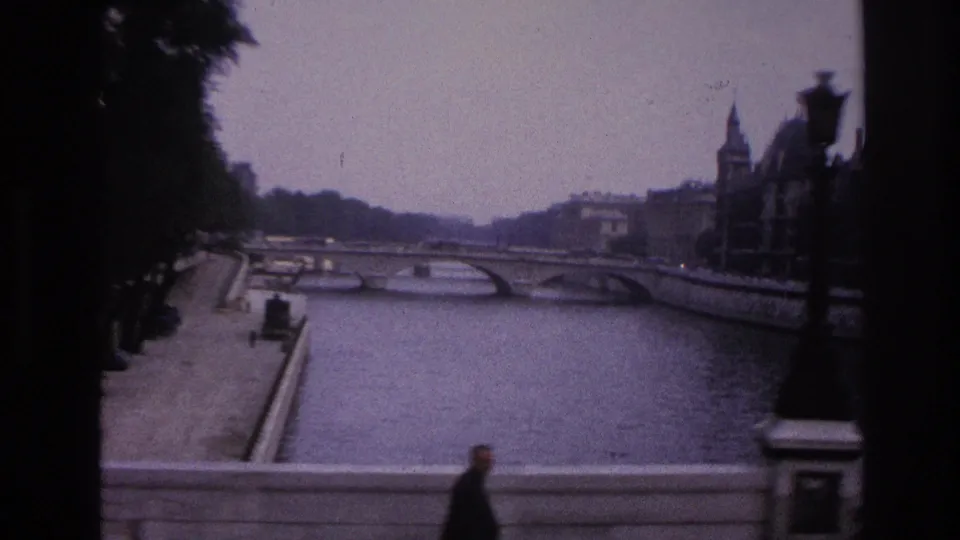 1967 Paris riverfront view with a stone bridge, embankment, ornate lamp, and a pedestrian passing near the lower edge.