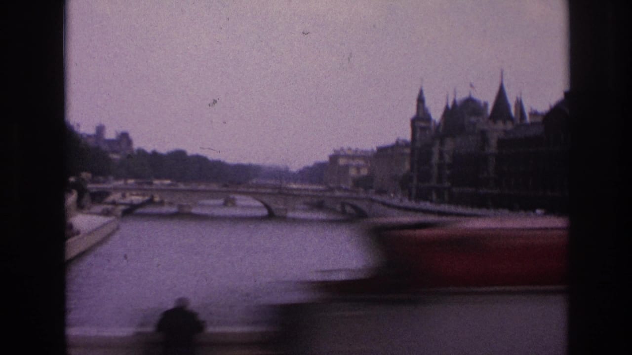 1967 Paris home-movie frame showing the Seine, a low bridge, historic riverside buildings, and a dark vehicle or window edge in the foreground.