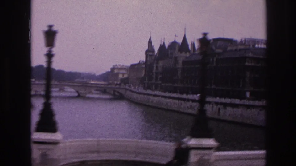 1967 Paris frame with a street lamp in front of the Seine, bridge railings, ornate riverside architecture, and a red blurred foreground detail.