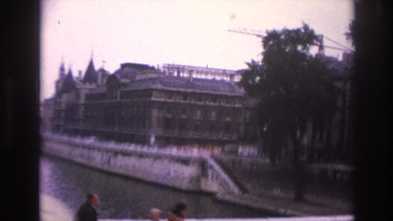 Paris, 1967, viewed from a moving car along the Seine, with riverside buildings, a stone quay, trees, a crane, and small pedestrians.