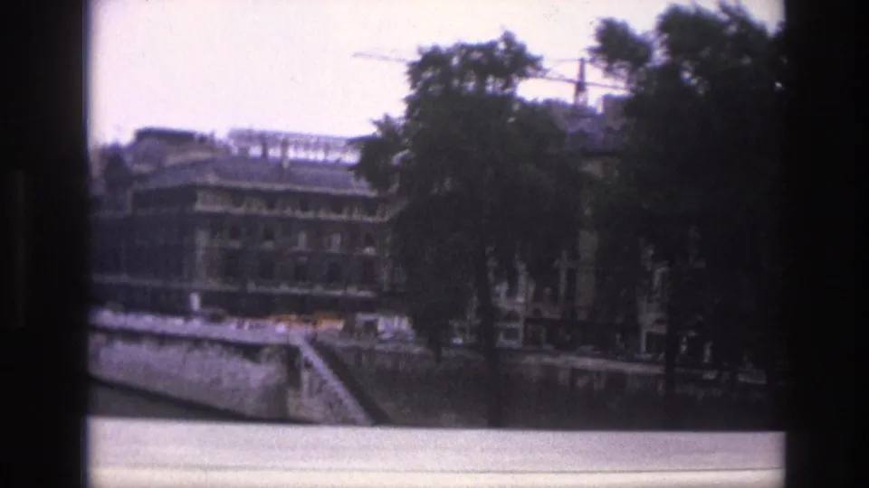 Soft 8mm frame from Paris showing the Seine embankment, riverside building, trees, steps to the quay, and a construction crane.