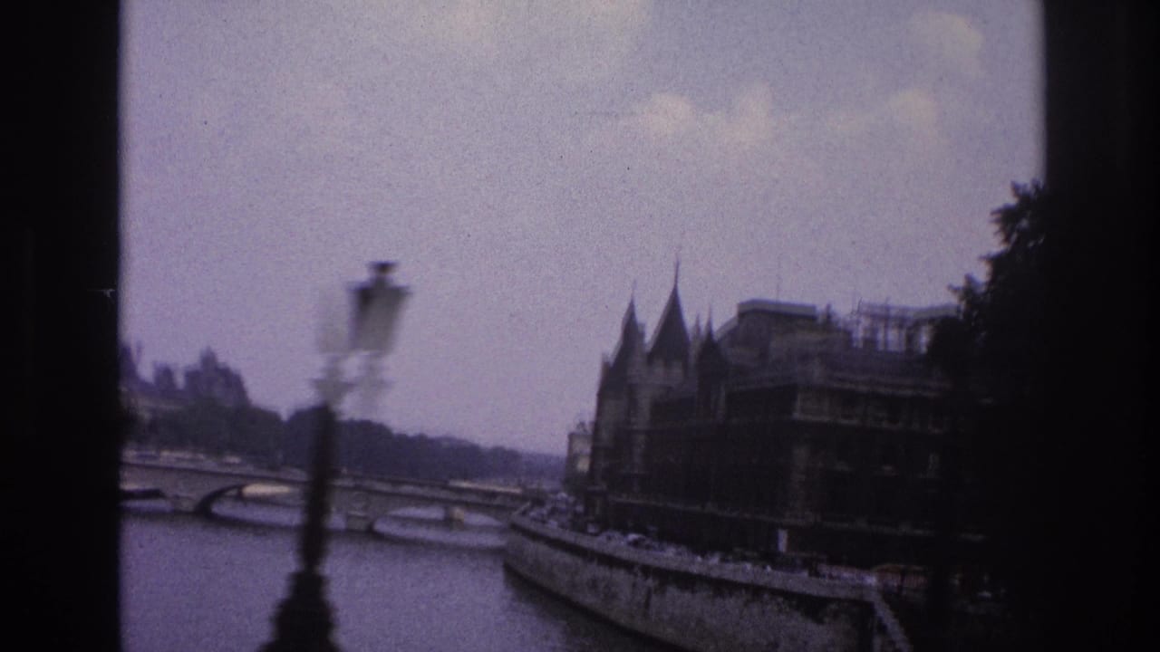 1967 Paris home-movie frame showing the Seine, a stone bridge, foreground lamppost, trees, and historic riverside architecture.