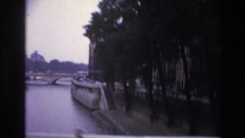 1967 Paris home-movie view of the Seine embankment, showing trees, a stone bridge, and soft 8mm exposure from a moving viewpoint.