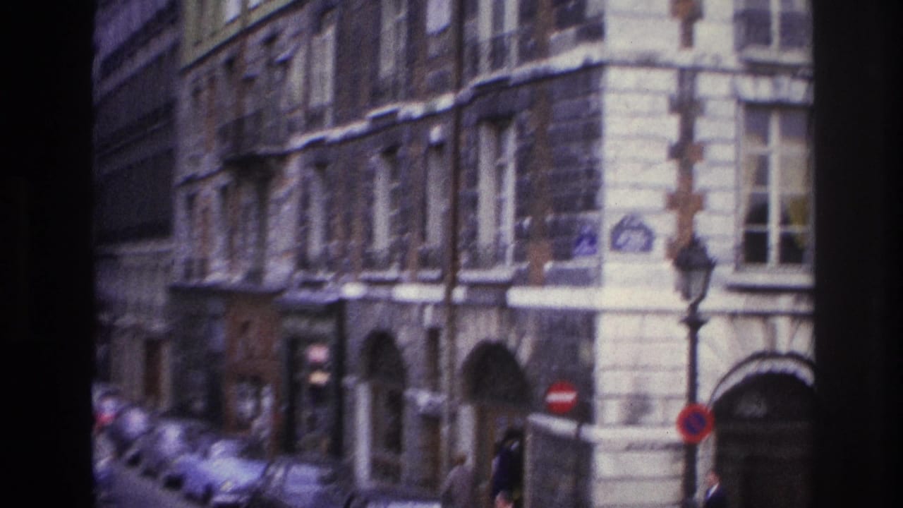 1967 Paris street view showing multi-story stone facades, arched entrances, parked cars, and a traffic sign near the corner.
