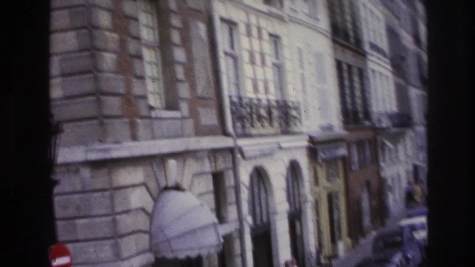 Paris building facade in 1967 with tall windows, balcony details, an arched doorway, and street signs at the curb.