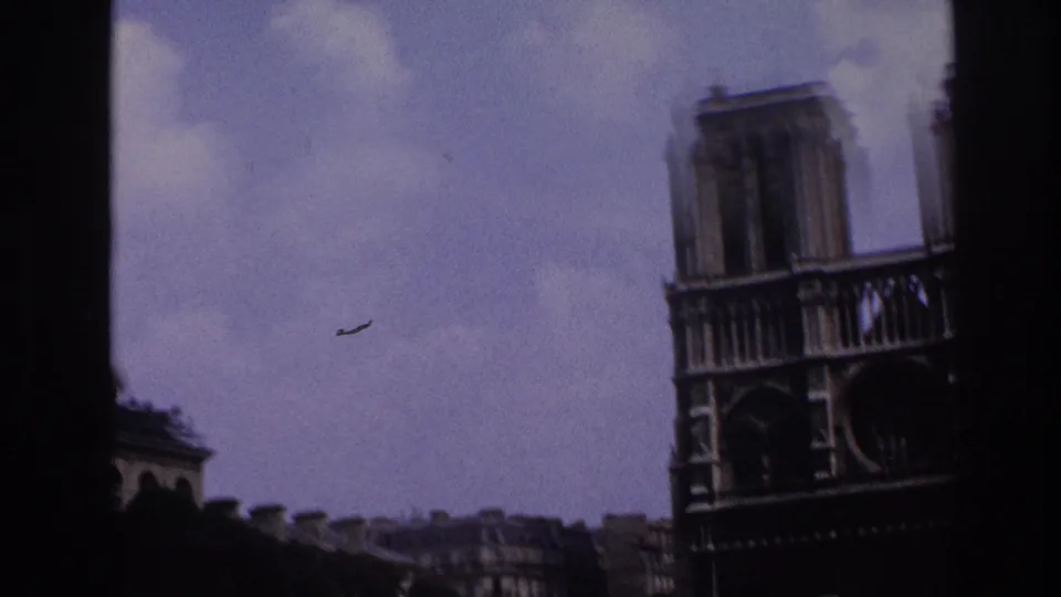 1967 Paris home-movie frame showing Notre-Dame Cathedral's facade from a moving vehicle, with soft focus and dark frame edges.