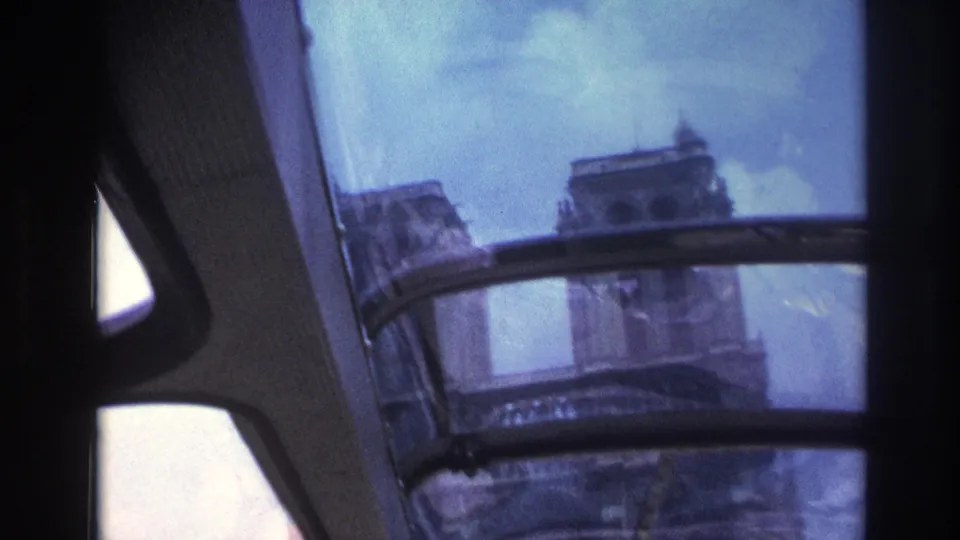 Notre-Dame's towers are seen through blue-tinted vehicle glass, with curved window trim and 8mm grain visible.