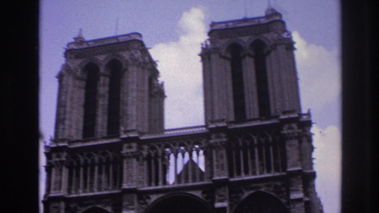 Low-angle 1967 Paris home-movie view of Notre-Dame's twin towers and upper facade against a pale sky.