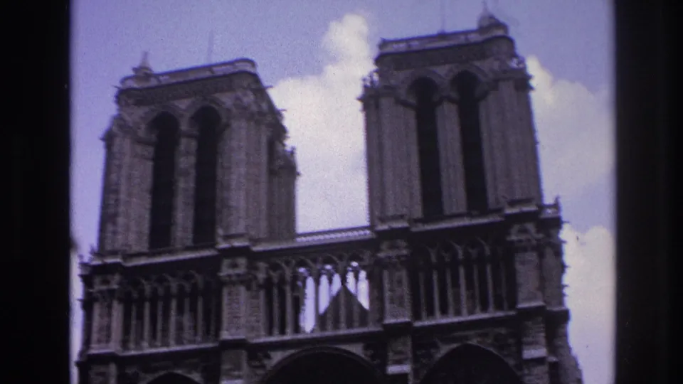 Low-angle 1967 Paris home-movie view of Notre-Dame's twin towers and upper facade against a pale sky.