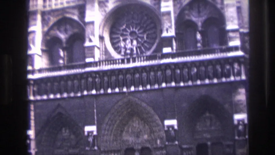 Handheld 1967 Paris frame of Notre-Dame's facade, including the rose window, Gothic arches, and shadowed entrance portals.