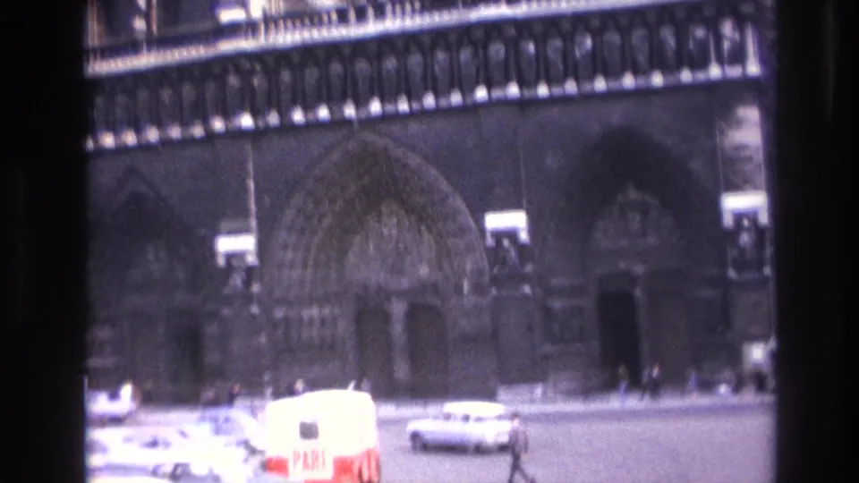 Street-level 1967 Paris view of Notre-Dame's main entrance with 1960s cars, a red-and-white marked van, and pedestrians.