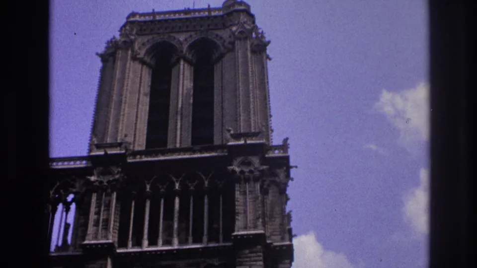 Visitor-shot upward view of Gothic cathedral towers in Paris, with dark stone detail and blue sky.