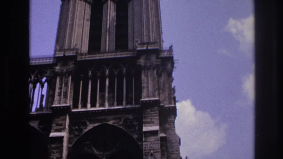 Close 1967 Paris home-movie view of Gothic cathedral tower details, with arches, columns, and sky behind.