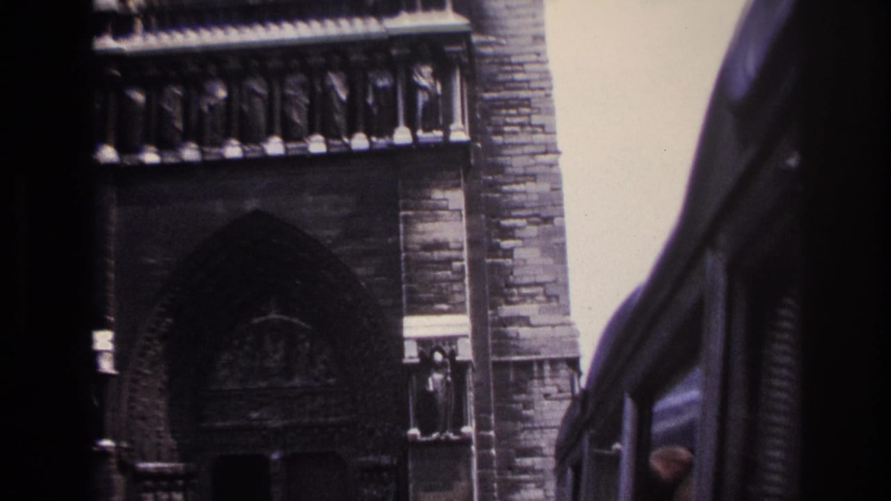 1967 Paris home-movie frame showing a Gothic cathedral facade partly obscured by the edge of a moving vehicle.