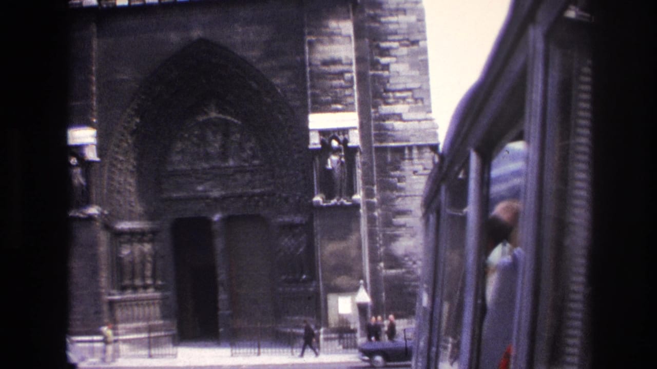 1967 Paris street view of a Gothic cathedral facade, seen from a moving vehicle with pedestrians near the entrance.