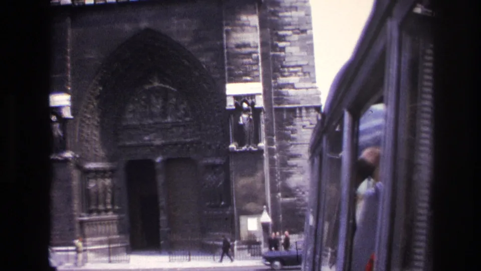 1967 Paris street view of a Gothic cathedral facade, seen from a moving vehicle with pedestrians near the entrance.