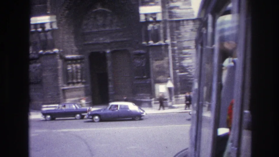 1967 Paris frame with classic cars on the street before a Gothic cathedral entrance and dark stone exterior.