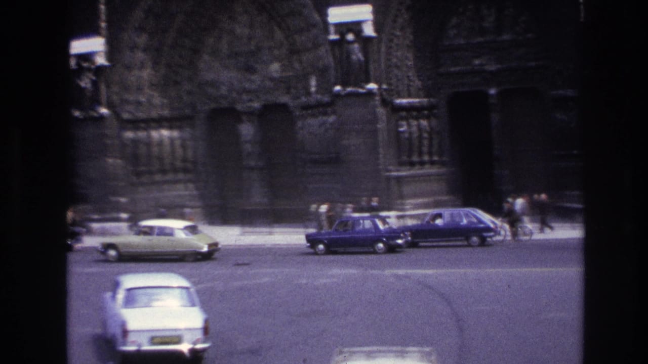 1967 Paris street view with small vintage cars crossing before a Gothic cathedral entrance and distant pedestrians.